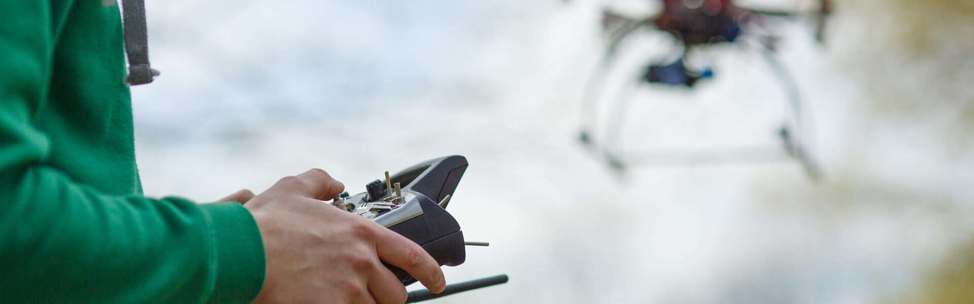 Persona con buzo verde controla un dron agrícola en vuelo mediante un control remoto, en un entorno natural al aire libre.