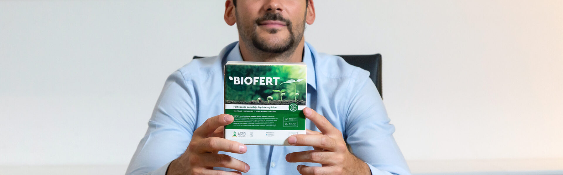 Joaquín Basanta sostiene un envase de BIOFERT frente a una mesa, vistiendo camisa celeste, en un entorno profesional con estantería al fondo.