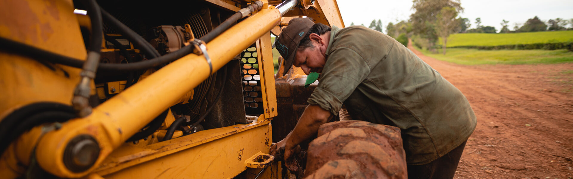 Agricultor realizando mantenimiento a maquinaria en un camino rural, como parte del trabajo de campo y adaptación tecnológica.