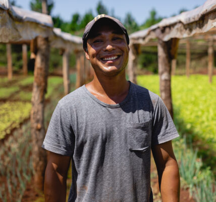 Agricultor sonriente en un invernadero rural, rodeado de cultivos protegidos, símbolo de agricultura sustentable y tecnologías aplicadas al campo.