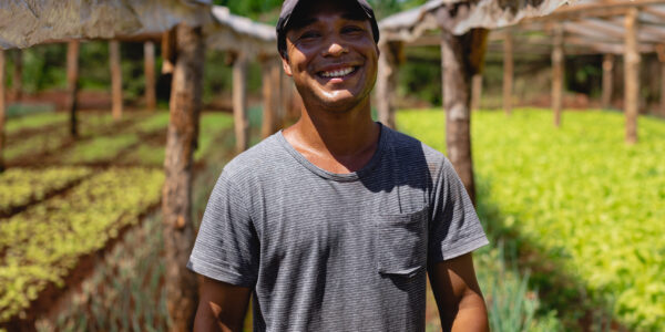 Agricultor sonriente en un invernadero rural, rodeado de cultivos protegidos, símbolo de agricultura sustentable y tecnologías aplicadas al campo.