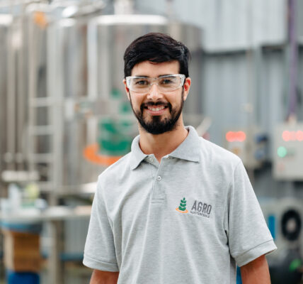 Técnico de Agro Sustentable con gafas de protección en planta de producción de bioinsumos, sonriendo frente a tanques industriales.