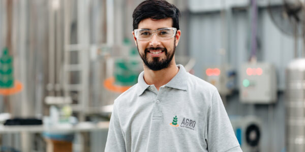 Técnico de Agro Sustentable con gafas de protección en planta de producción de bioinsumos, sonriendo frente a tanques industriales.