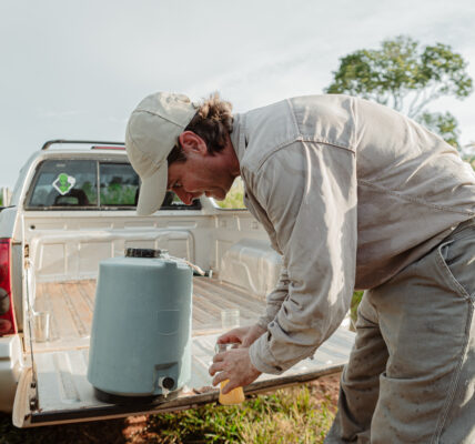 Productor rural prepara bioinsumos naturales desde la caja de una camioneta en medio del campo, en un entorno de vegetación y cielo despejado.