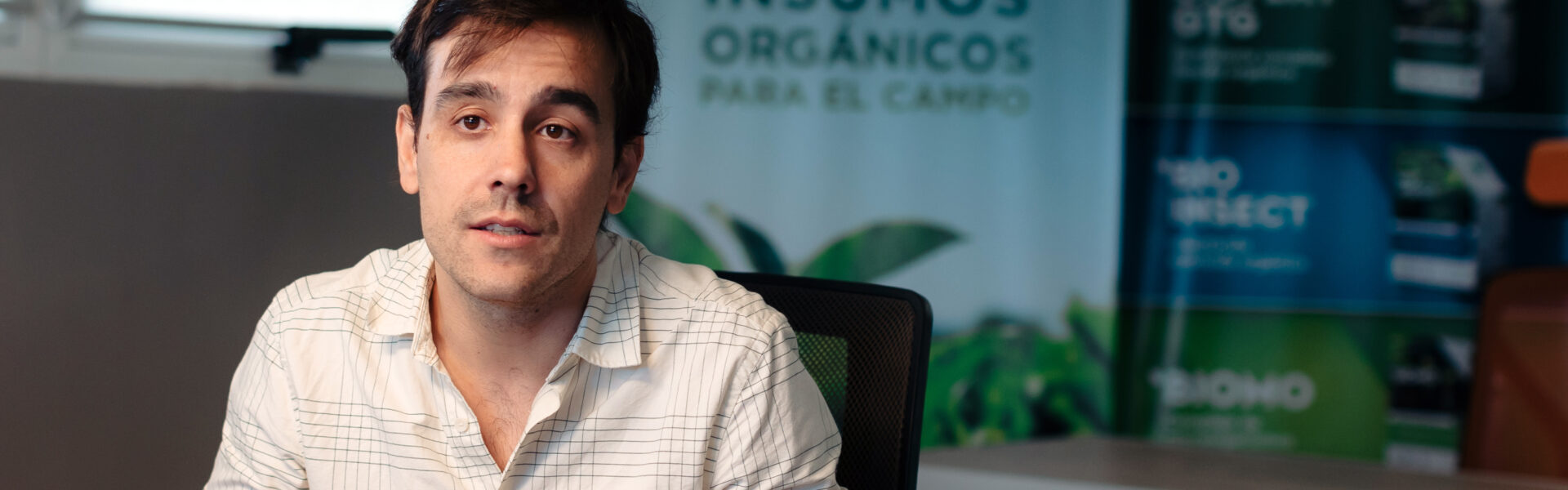 Matías Imperiale habla en una oficina sobre prácticas agrícolas sustentables, con afiches de Agro Sustentable de fondo.