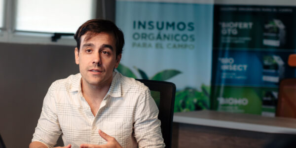 Matías Imperiale habla en una oficina sobre prácticas agrícolas sustentables, con afiches de Agro Sustentable de fondo.