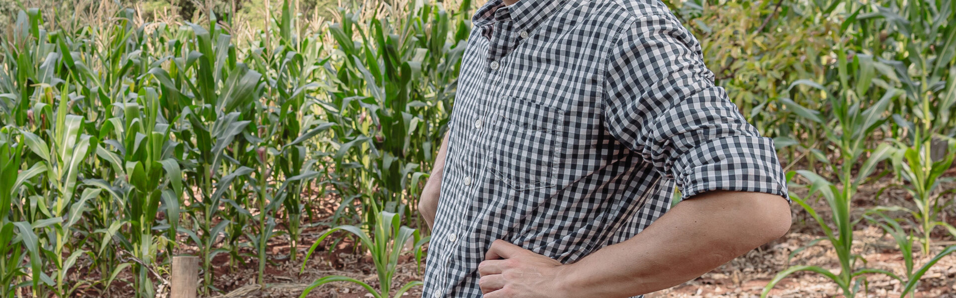 Matías Imperiale en un cultivo de maíz, con camisa a cuadros y jeans, observando el campo rodeado de vegetación.