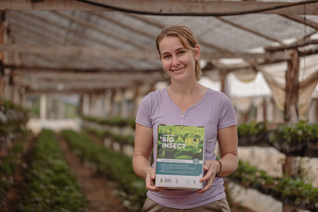 Productora rural sostiene una caja de BIOINSECT en un invernadero, mostrando su compromiso con prácticas agrícolas ecológicas promovidas por Agro Sustentable.