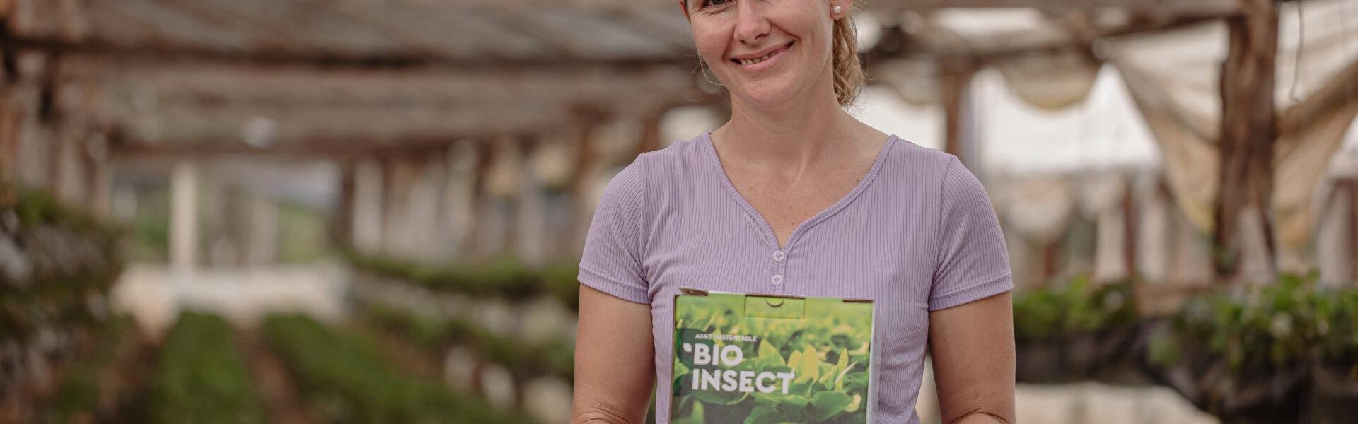 Productora rural sostiene una caja de BIOINSECT en un invernadero, mostrando su compromiso con prácticas agrícolas ecológicas promovidas por Agro Sustentable.