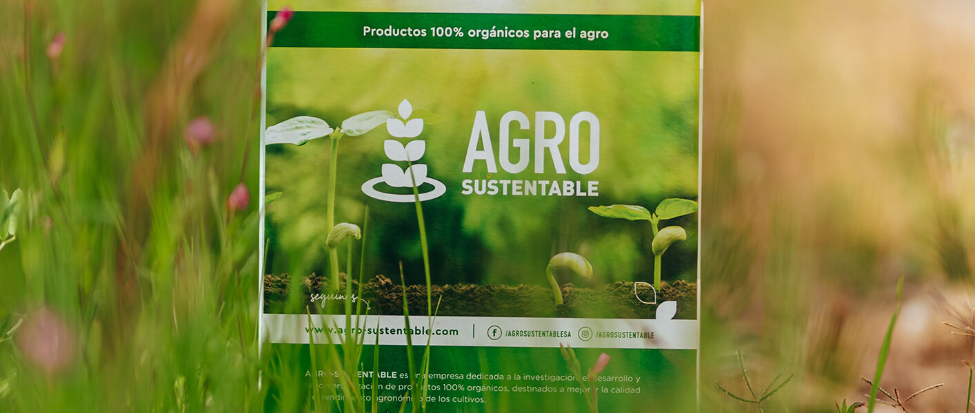 Envase de productos orgánicos de Agro Sustentable colocado en un campo natural con vegetación verde y flores silvestres.