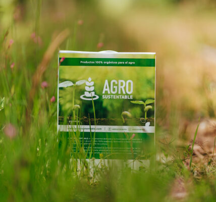 Envase de productos orgánicos de Agro Sustentable colocado en un campo natural con vegetación verde y flores silvestres.