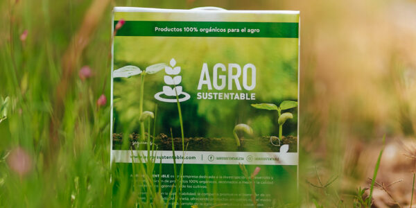 Envase de productos orgánicos de Agro Sustentable colocado en un campo natural con vegetación verde y flores silvestres.