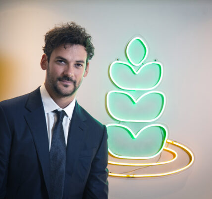 Hombre con traje posa frente al logo iluminado de una empresa agroindustrial, simbolizando innovación tecnológica en el sector agrícola.