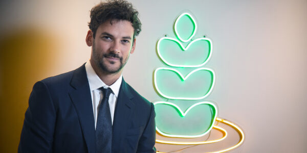 Hombre con traje posa frente al logo iluminado de una empresa agroindustrial, simbolizando innovación tecnológica en el sector agrícola.