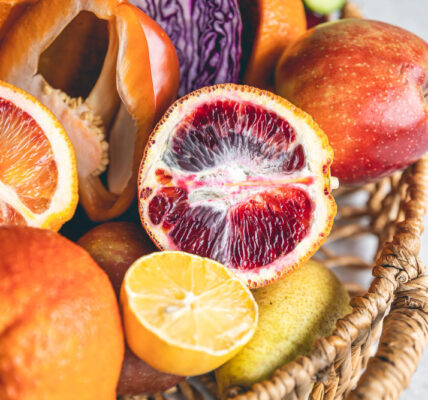 Canasta con frutas frescas y cortadas como naranja sanguina, limón, manzana y otras, mostrando variaciones de color, pulpa y textura asociadas a la maduración.